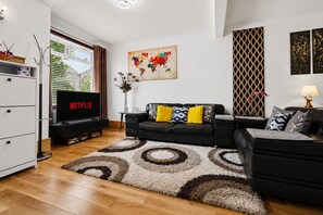 A modern living room with a black leather sofa, a flat-screen TV displaying 'NETFLIX', a decorative world map, and a patterned rug. - Easy London Links | Tottenham Stadium | Drumsheds (Greater London)