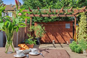 A patio with a wooden pergola, potted plants, a small dog, and a table with croissants and cups. - Easy London Links | Tottenham Stadium | Drumsheds (Greater London)