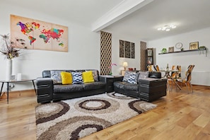 A modern living room with a sectional sofa, a world map artwork, decorative panels, and a dining area with chairs and a table. - Easy London Links | Tottenham Stadium | Drumsheds (Greater London)