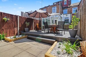 A patio with a table and chairs, a wooden fence, and potted plants. - Easy London Links | Tottenham Stadium | Drumsheds (Greater London)