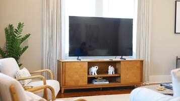 Un salon avec un téléviseur à écran plat posé sur un meuble en bois, deux statuettes d’éléphants blanches, une plante en pot et un canapé avec des coussins.