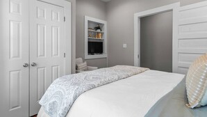 A bedroom with a bed, a wardrobe, a shelf with decorative items, and a door. - Fourth & Tide on 8th• Walk • Stay • Roll Tide (Tuscaloosa)