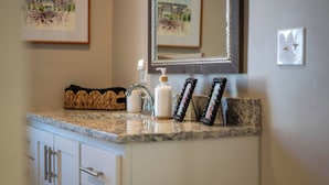 A bathroom with a granite countertop, a mirror, a soap dispenser, and framed pictures on the wall. - Fourth & Tide on 8th• Walk • Stay • Roll Tide (Tuscaloosa)