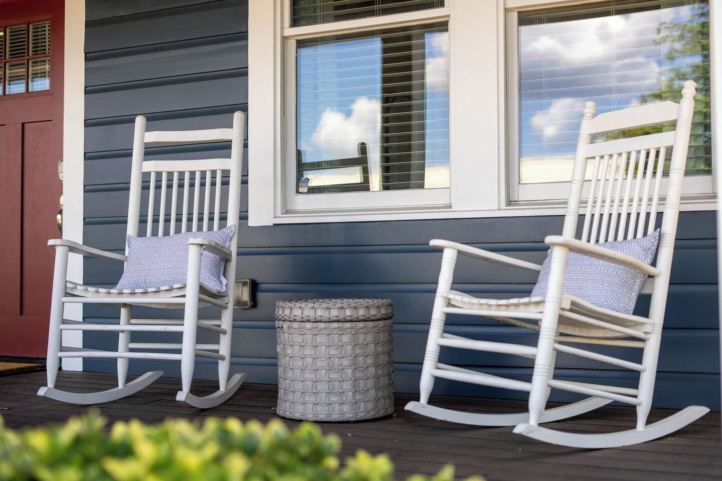 Two rocking chairs on a porch with a window and a door.