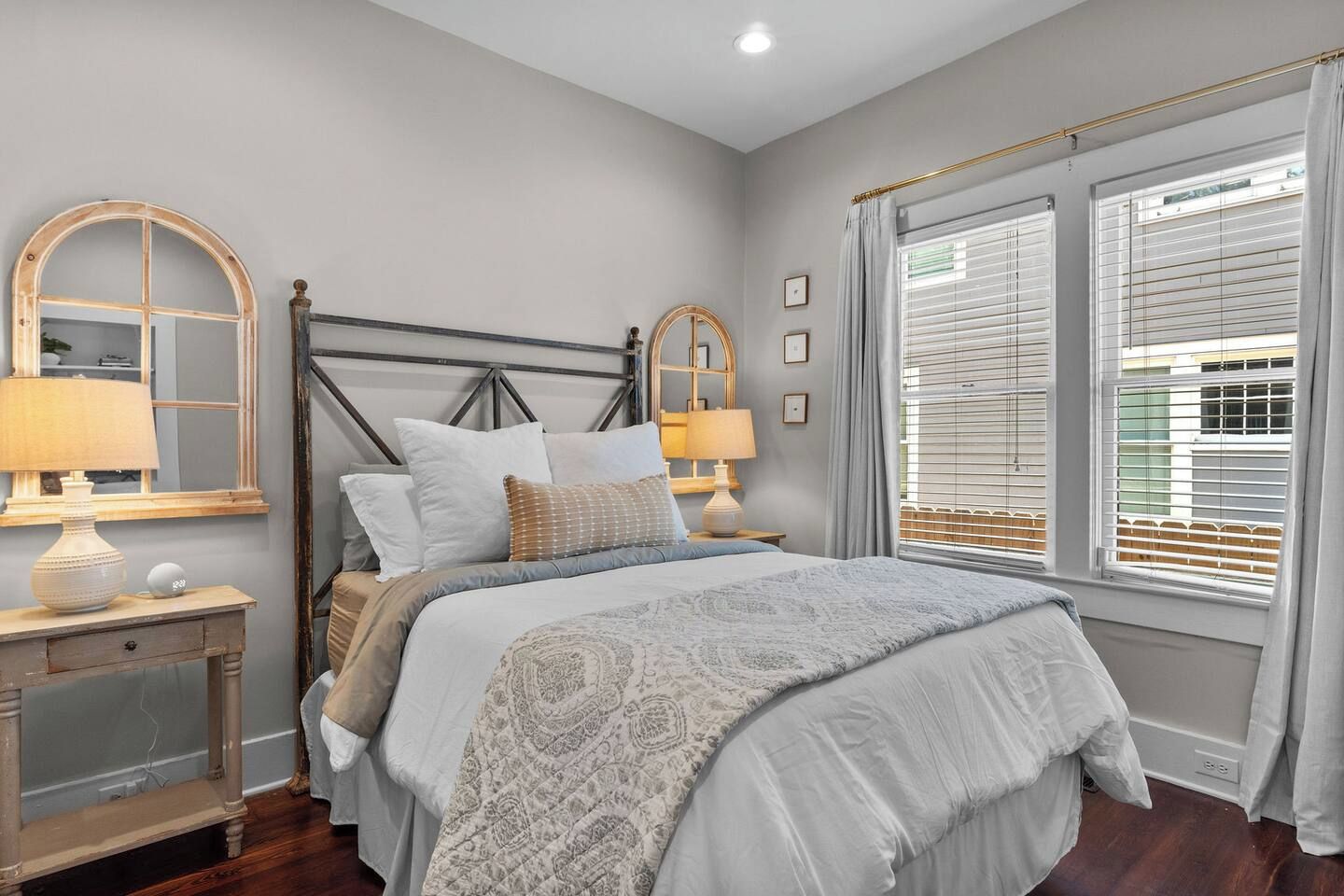 Quarto com cama, mesas de cabeceira, luminárias e janela com persianas.