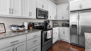 A modern kitchen with white cabinets, stainless steel appliances, and a granite countertop. - Fourth & Tide on 8th• Walk • Stay • Roll Tide (Tuscaloosa)