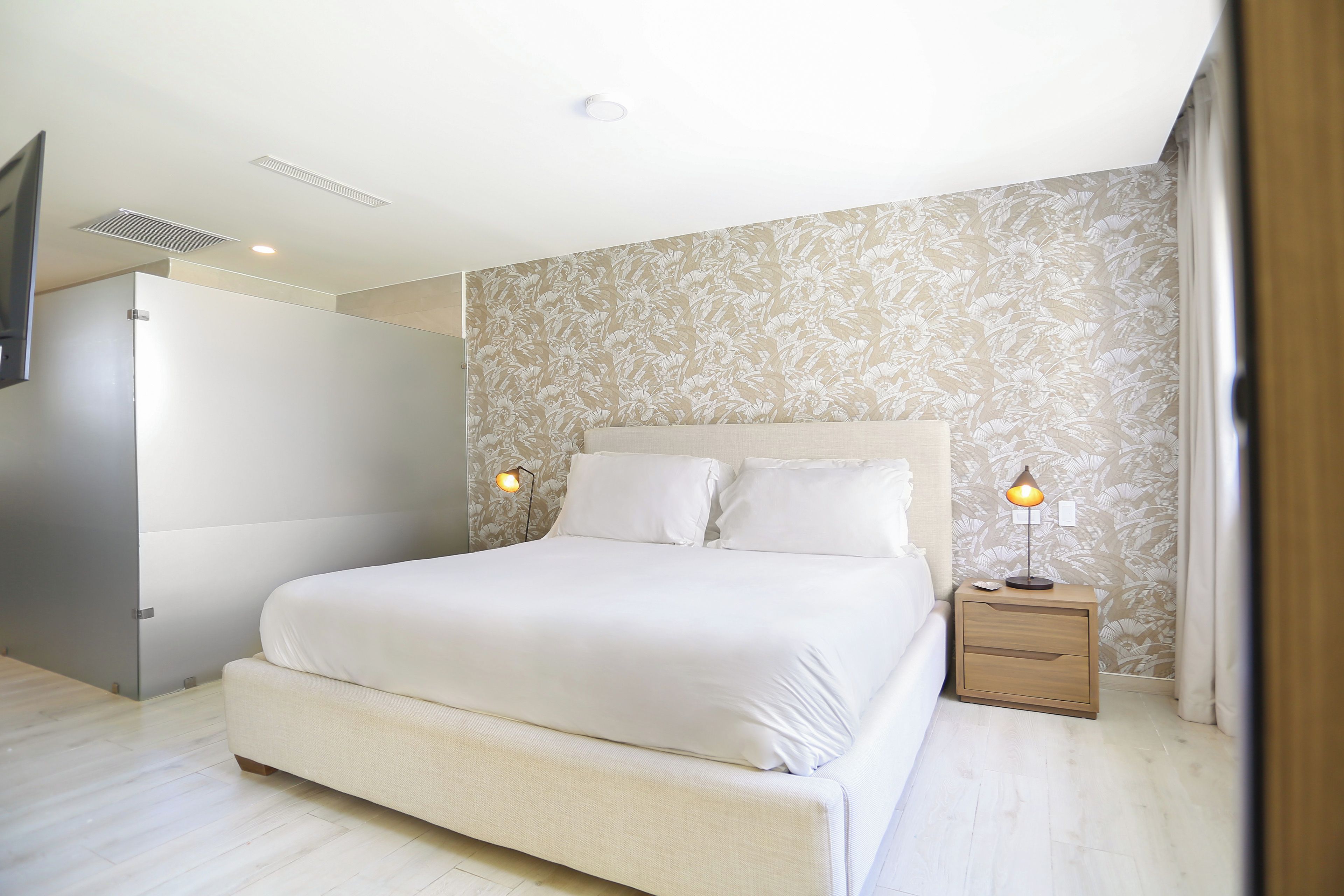 Un dormitorio con una cama grande, lámparas de noche y un papel tapiz estampado.