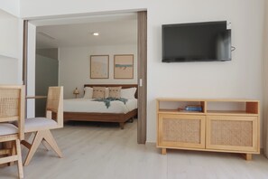 A bedroom with a bed, a TV mounted on the wall, a wooden cabinet, and a chair.