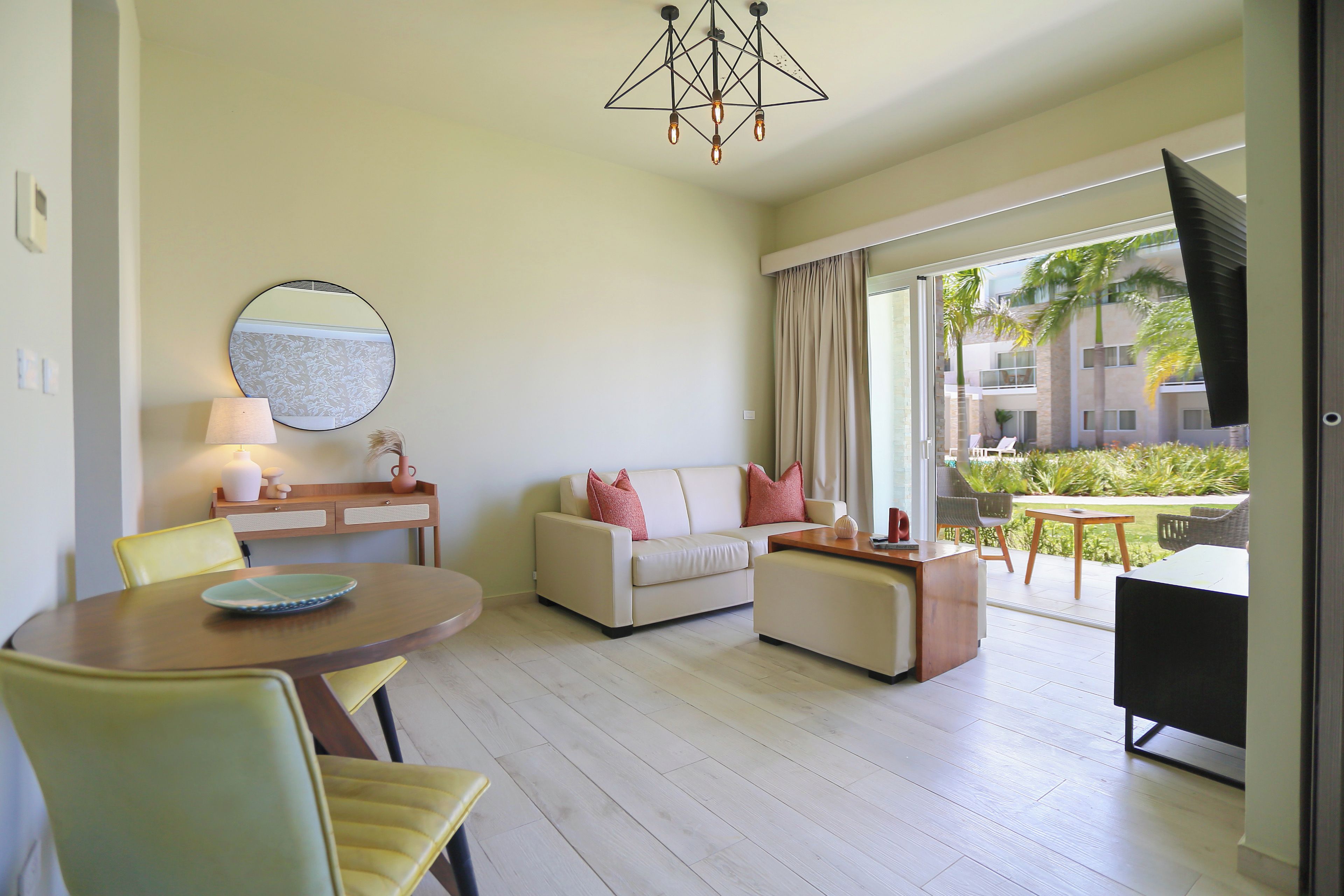 A modern living room with a sofa, chairs, a dining table, and a large window with a view of a building and greenery.