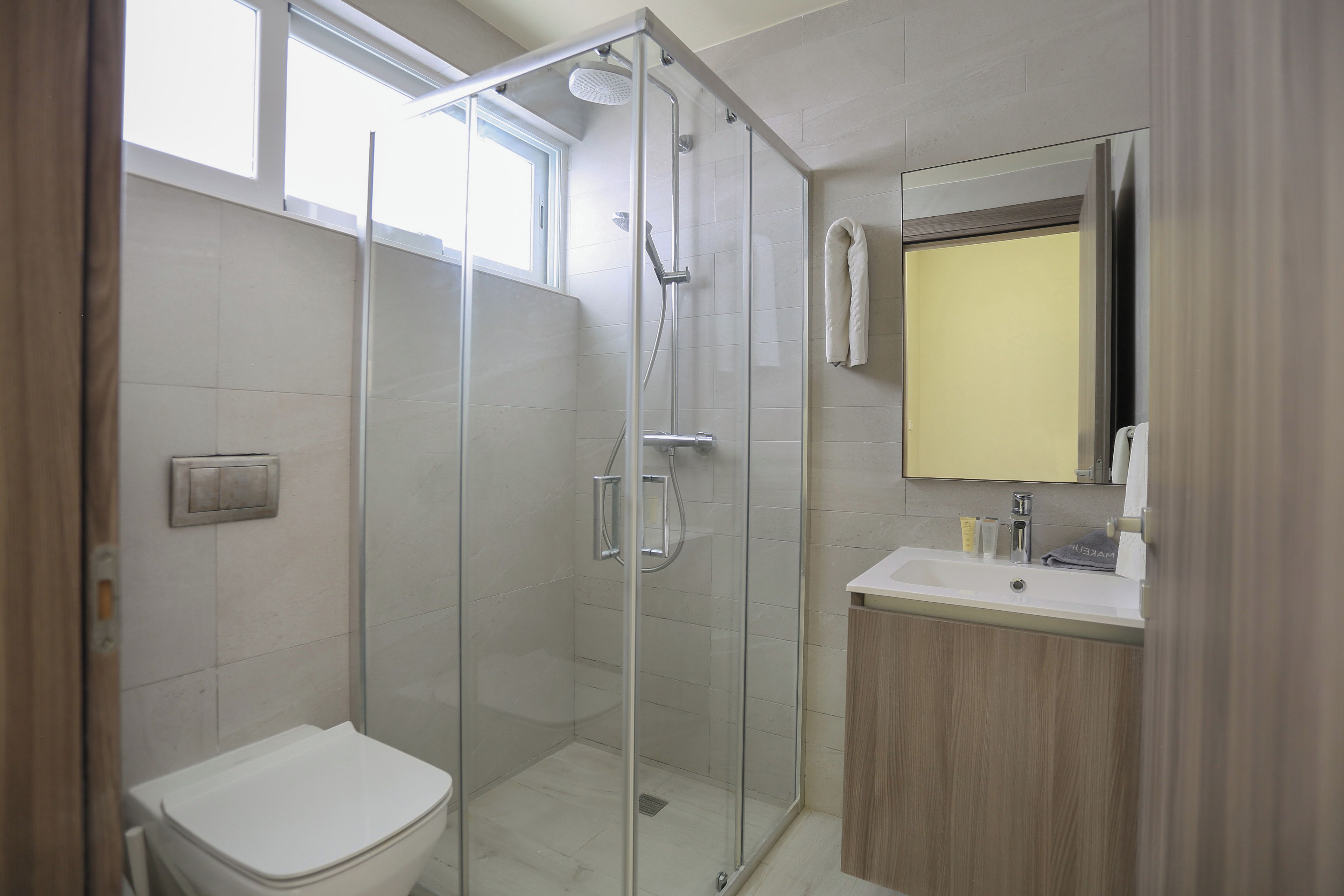 A modern bathroom with a glass-enclosed shower, a toilet, and a sink with a mirror above it.