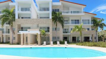 A multi-story hotel with a swimming pool, palm trees, and a clear blue sky.