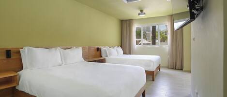 A hotel room with two beds, wooden headboards, a window with curtains, and a ceiling fan.