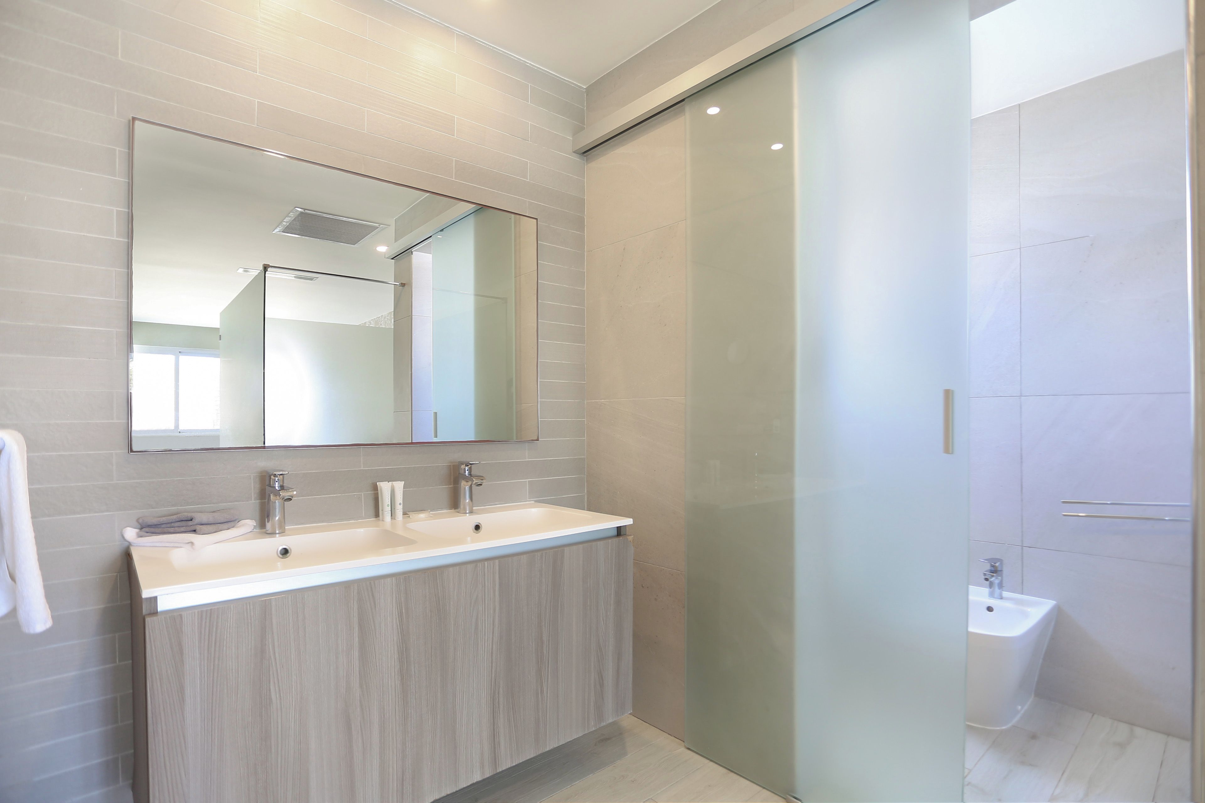 Un baño moderno con un espejo grande, dos lavamanos y una zona de ducha.
