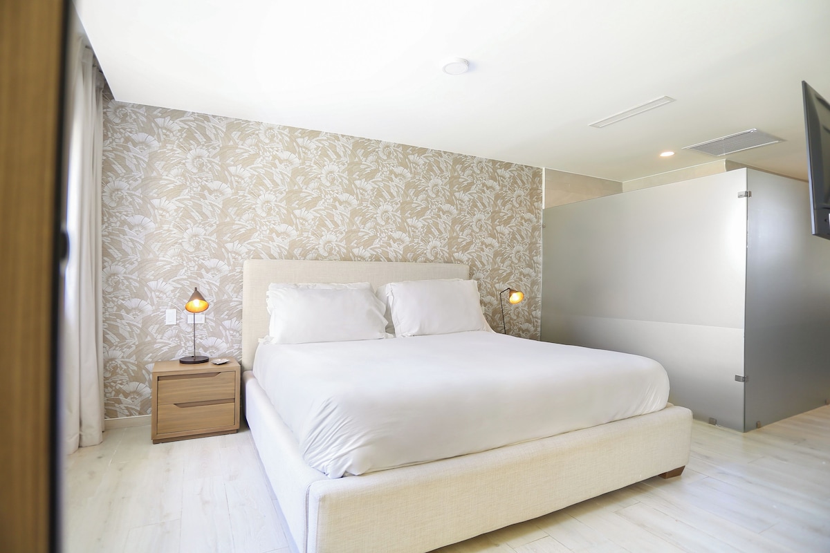 Un dormitorio moderno con una cama grande, dos lámparas de noche y un papel tapiz estampado.