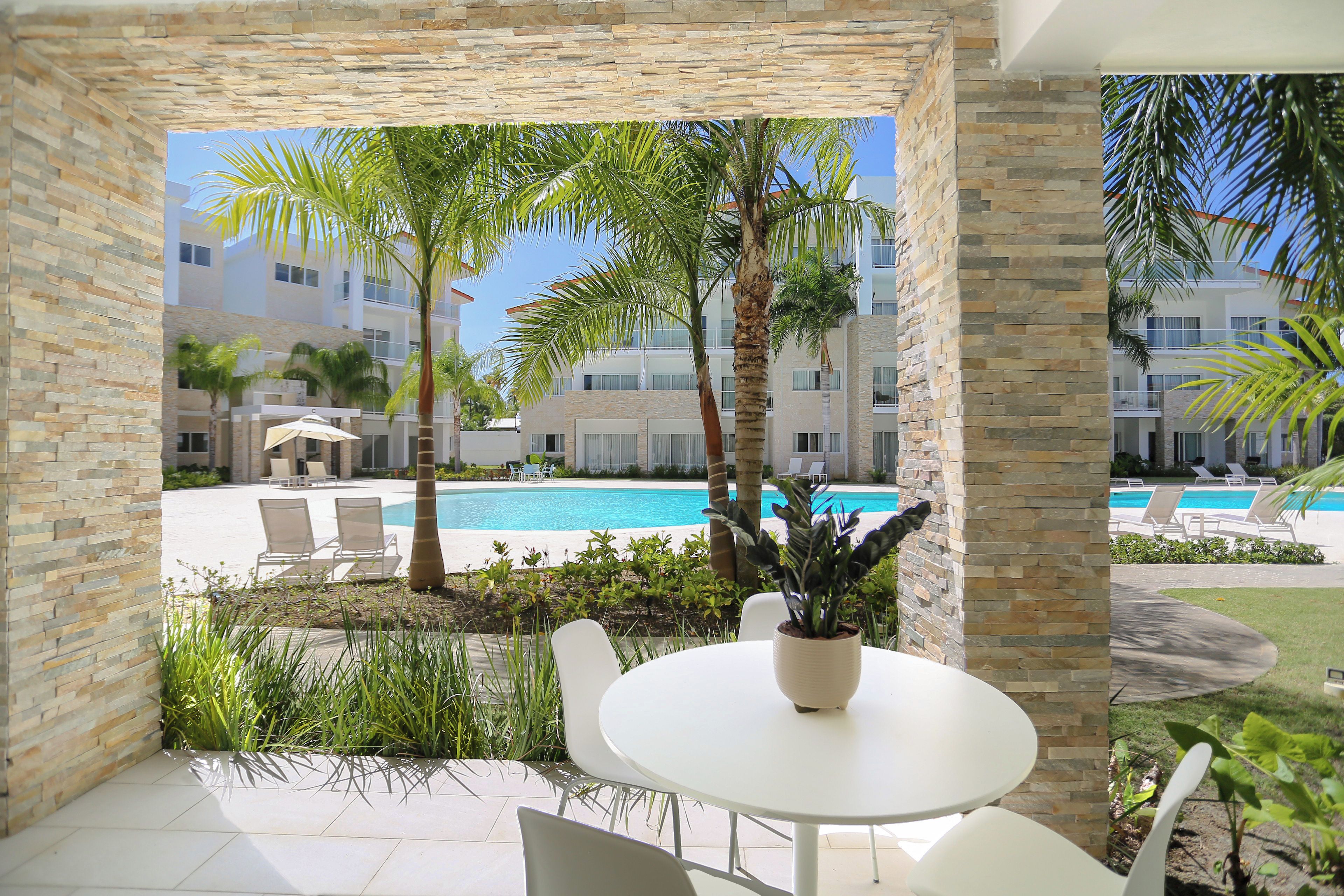 Un patio con mesa y sillas, con vista a una piscina y un edificio con balcones.