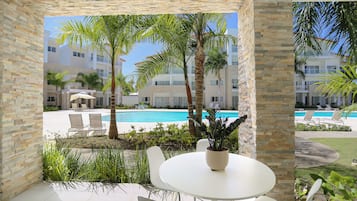 Un patio con mesa y sillas, con vista a una piscina y un edificio con balcones.