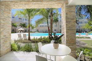 Un patio con mesa y sillas, con vista a una piscina y un edificio con balcones.