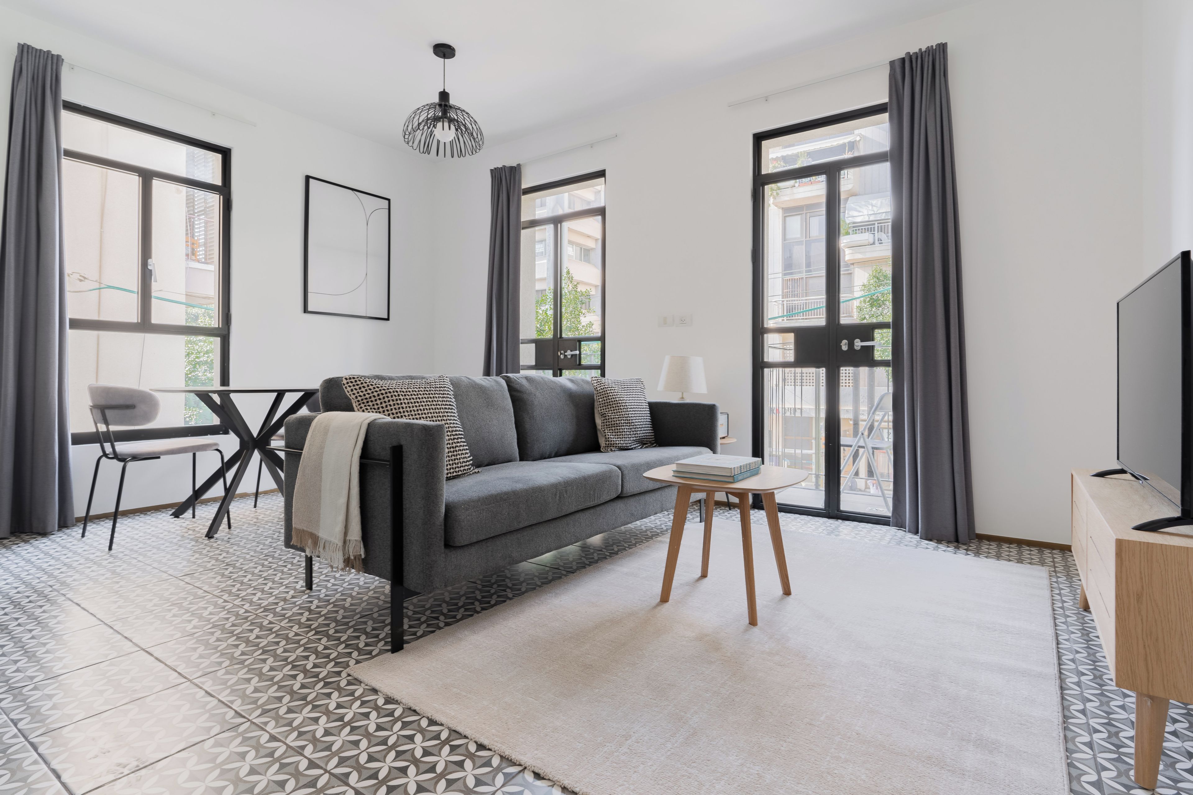 Una sala de estar moderna con un sofá gris, una mesita redonda y un televisor sobre un mueble de madera.