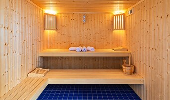 Una sauna con paredes de madera, un banco, un banco con toallas y un cubo de madera.