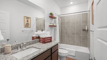 A modern bathroom with a granite countertop, a toilet, a bathtub, and a shower area.