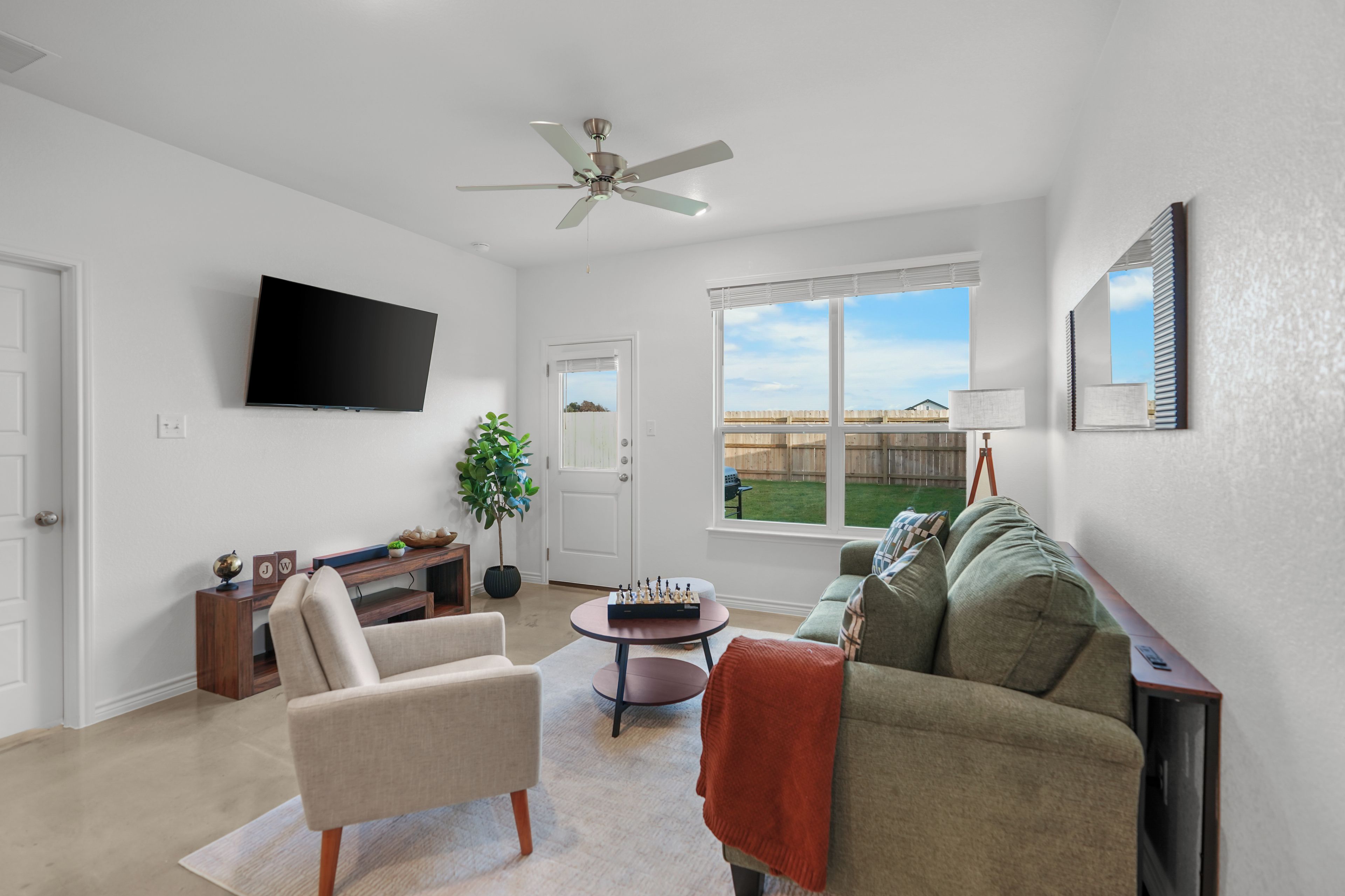 A living room with a flat-screen TV, a ceiling fan, a sofa, a coffee table, and a view of a backyard.