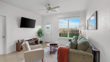 A living room with a flat-screen TV, a ceiling fan, a sofa, a coffee table, and a view of a backyard.
