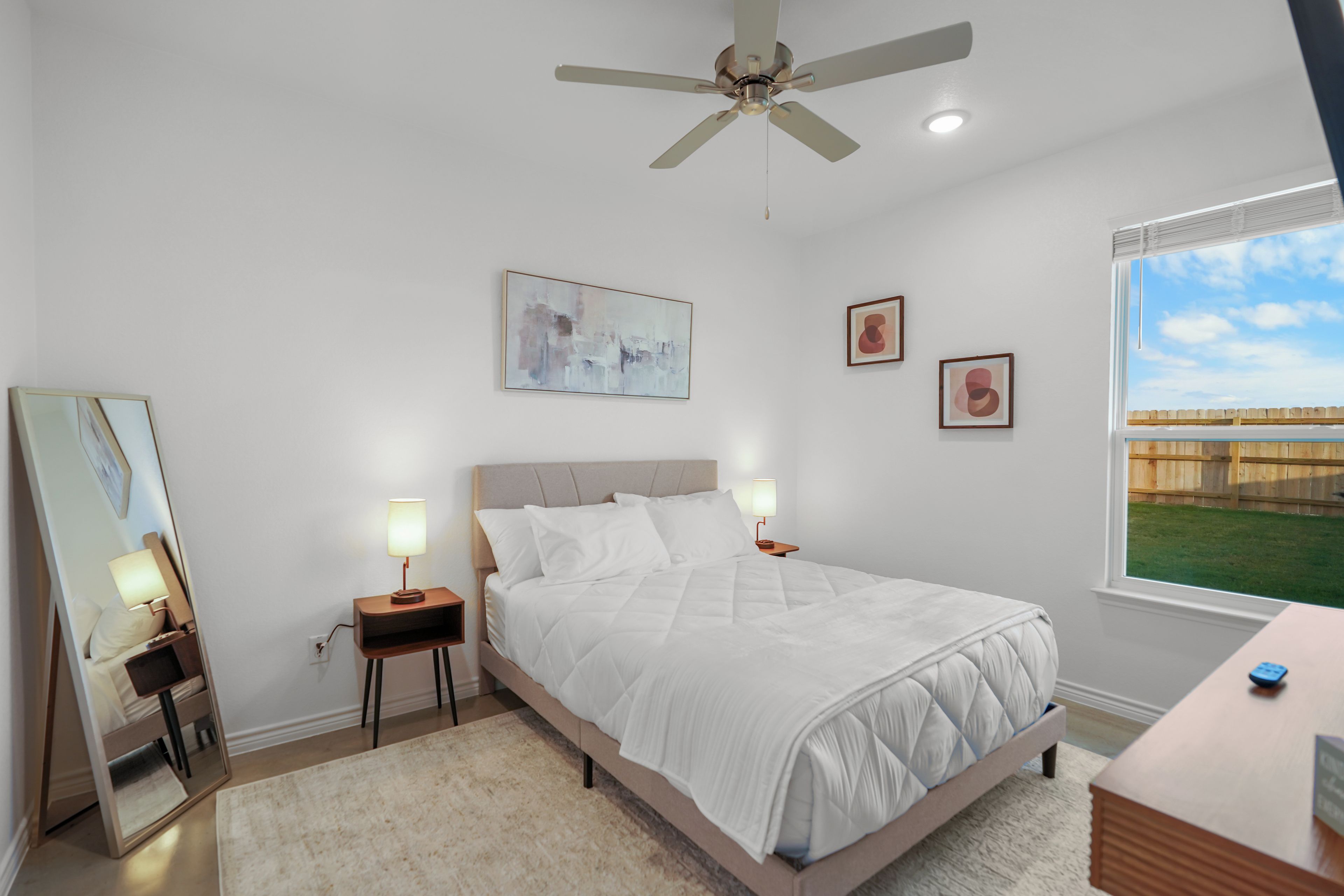Un dormitorio con cama, mesitas de noche, ventilador de techo y obras de arte en las paredes.