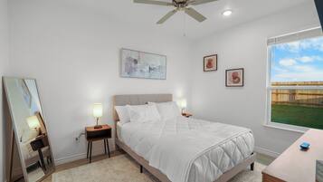 Un dormitorio con cama, mesitas de noche, ventilador de techo y obras de arte en las paredes.