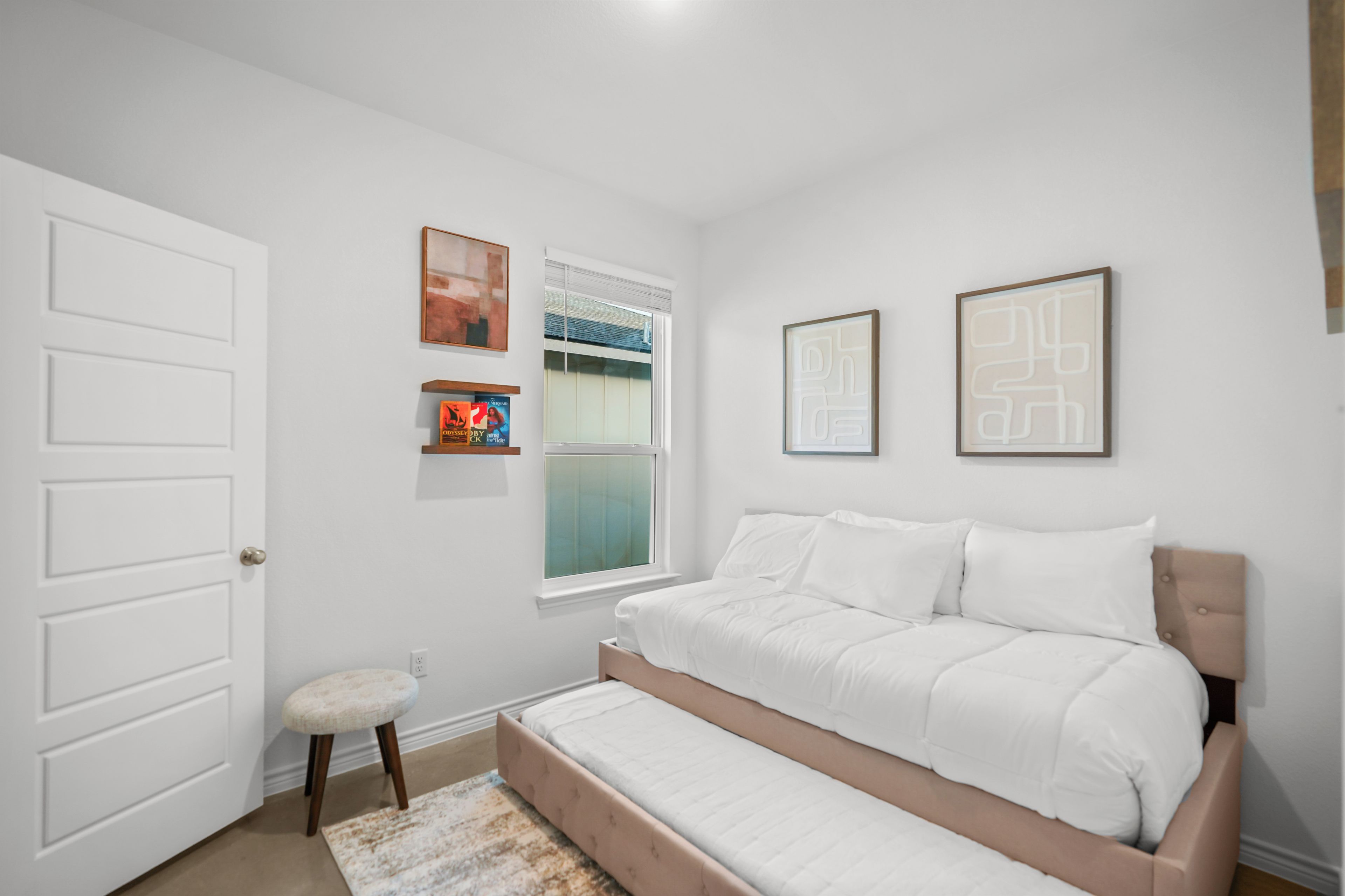 A bedroom with a bed, a window, a door, and wall-mounted artwork.