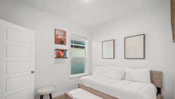 A bedroom with a bed, a window, a door, and wall-mounted artwork.