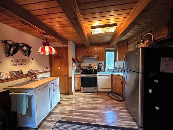 Een keuken met houten kastjes, een centraal eiland, een koelkast en een plafondlamp.
