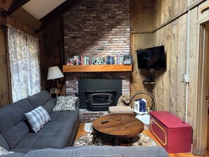 Een gezellige woonkamer met een bank, een open haard, een televisie en een boekenplank.
