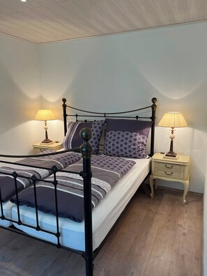 A single bed with a metal frame, two bedside tables with lamps, and a patterned bedspread. - Ilztalperle – A Modern Getaway Right on the Ilz River in the Bavarian Forest (Hutthurm)