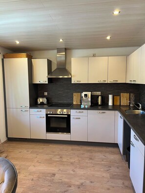 A modern kitchen with white cabinets, a black countertop, and a stainless steel range hood. - Ilztalperle – A Modern Getaway Right on the Ilz River in the Bavarian Forest (Hutthurm)