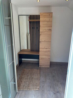 A compact room with a built-in wardrobe, a small bench, and a woven rug. - Ilztalperle – A Modern Getaway Right on the Ilz River in the Bavarian Forest (Hutthurm)