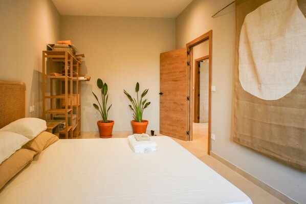 A bedroom with a bed, two potted plants, a wooden ladder, and a door.