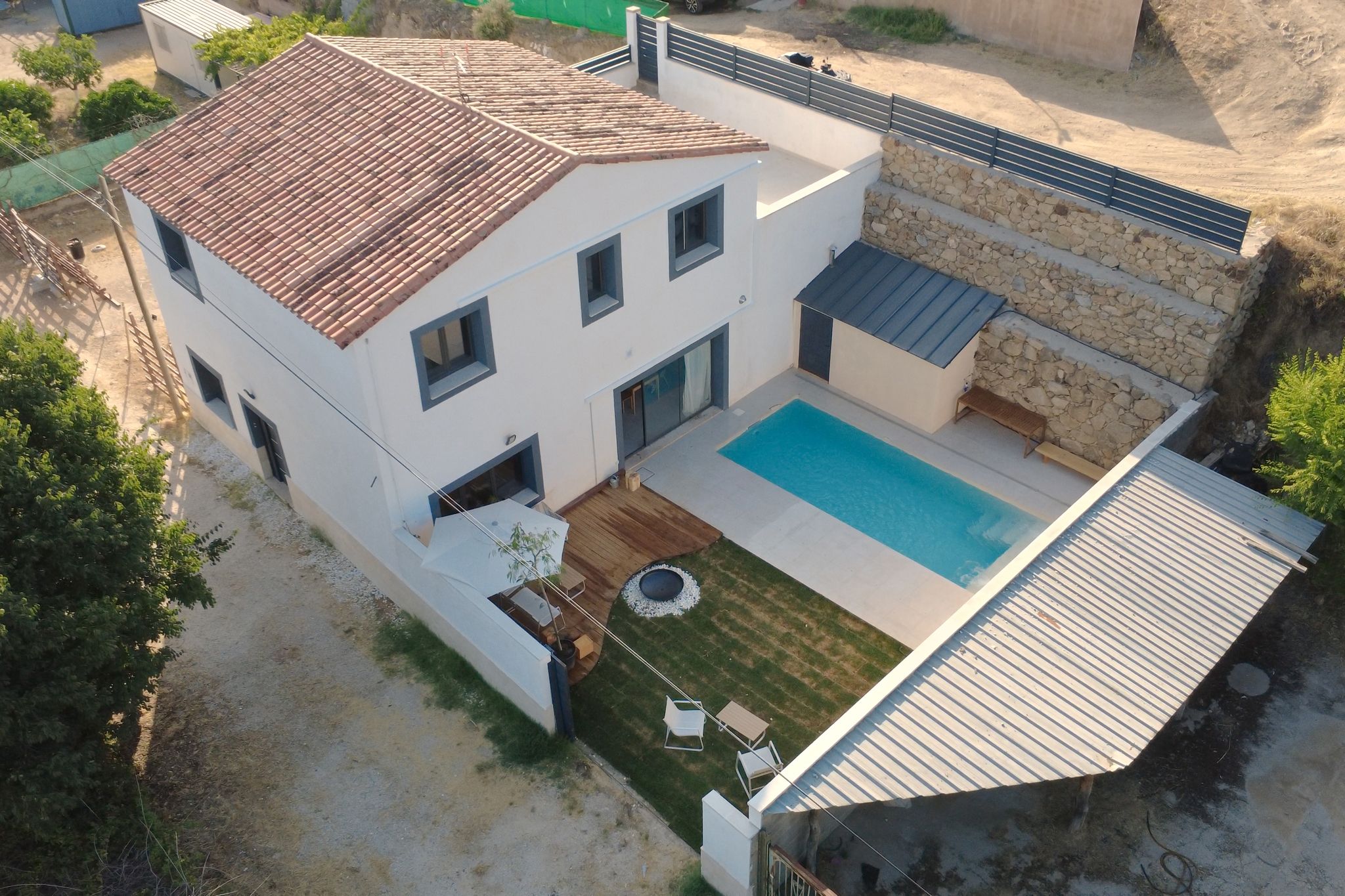 Une maison à deux étages avec une piscine, un patio doté de mobilier d’extérieur et un mur de soutènement en pierre.