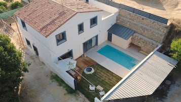Une maison à deux étages avec une piscine, un patio doté de mobilier d’extérieur et un mur de soutènement en pierre.