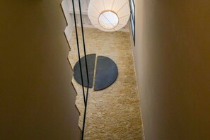 A hallway with a stone floor, a circular dark rug, and a hanging light fixture.