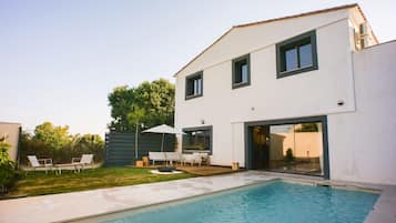 Une maison moderne à deux étages, dotée d’une piscine, d’un espace salon extérieur et d’un grand arbre.