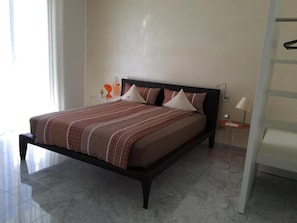 Un llit amb un estovat estampat, una taula de nit amb una làmpada i una cadira.