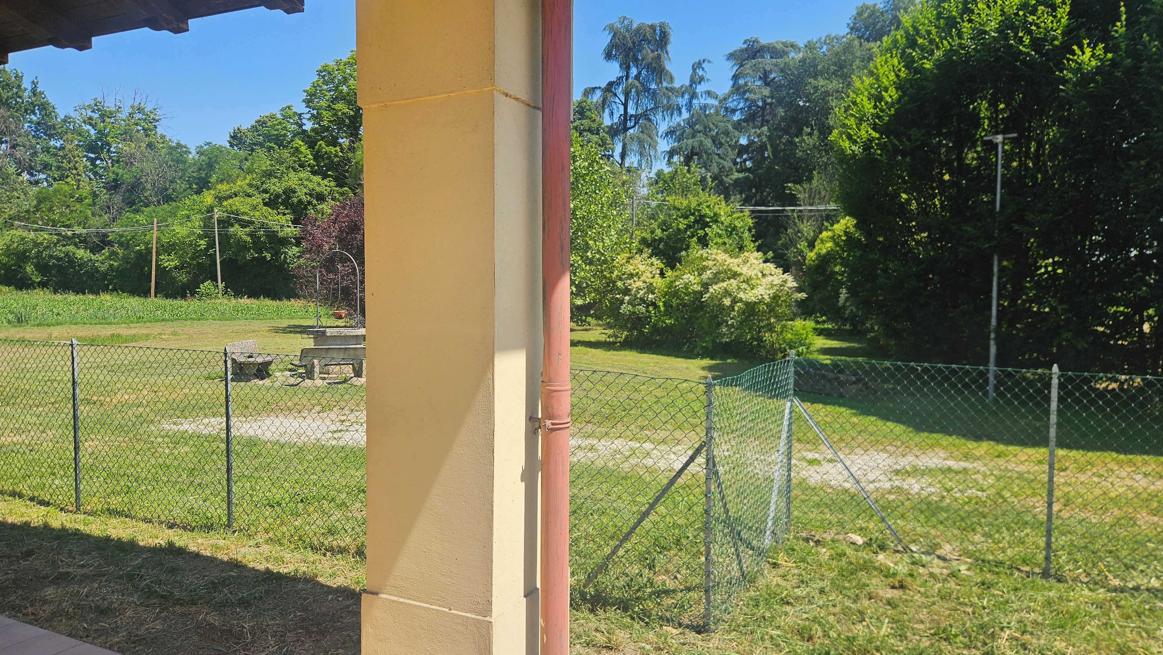 A fenced outdoor area with a picnic table and benches, surrounded by greenery and trees.