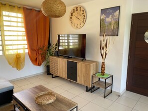 A living room with a television on a wooden cabinet, a clock on the wall, and a door. - Just like at home!! A quiet and pleasant apartment with a balcony overlooking the forest (none)