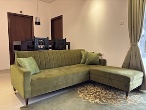 A green sofa with a patterned rug, wooden chairs, and a window with curtains. - Spacious 3-bedroom apartment with AC in gorgeous Chicalim (Chicalim)