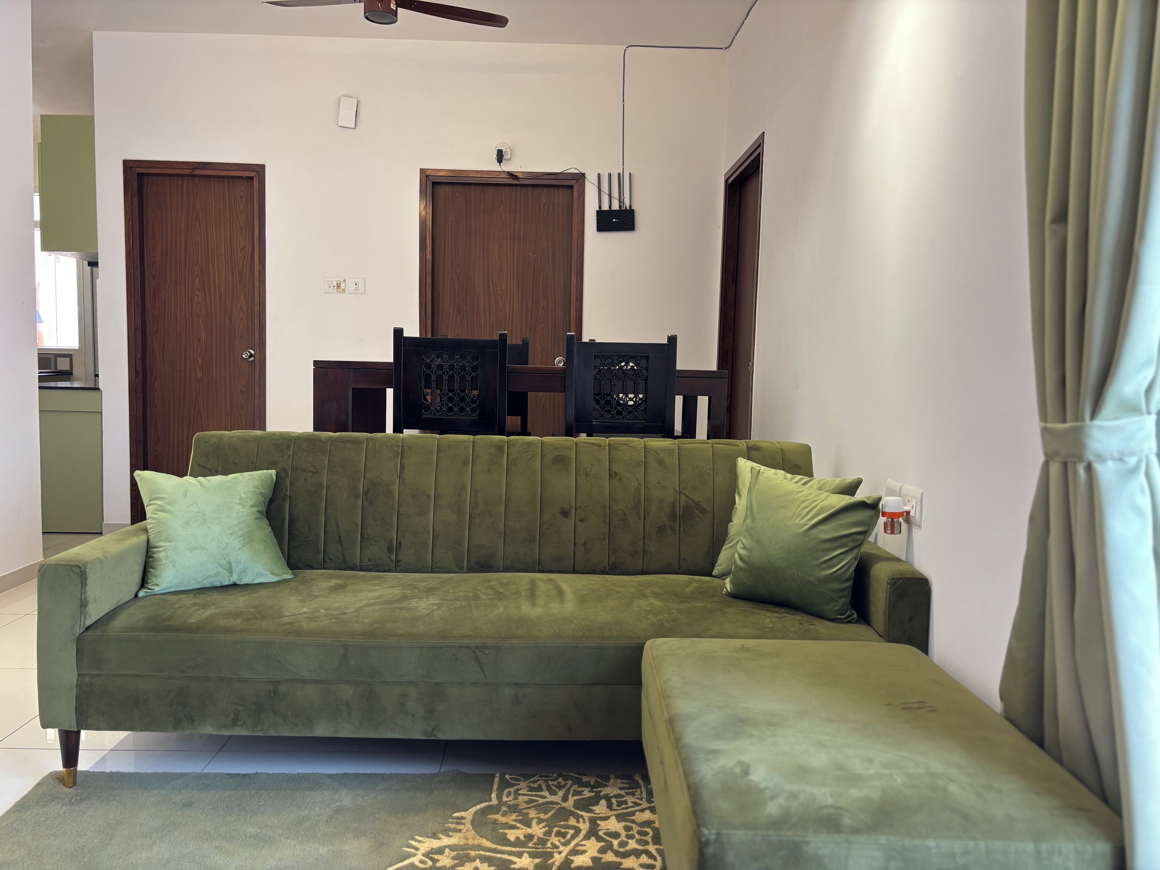 A living room with a green sofa, a patterned rug, and a dining area with chairs and a table.