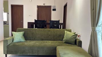 A living room with a green sofa, a patterned rug, and a dining area with chairs and a table.