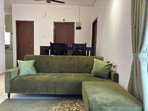 A living room with a green sofa, a patterned rug, and a dining area with chairs and a table. - Spacious 3-bedroom apartment with AC in gorgeous Chicalim (Chicalim)