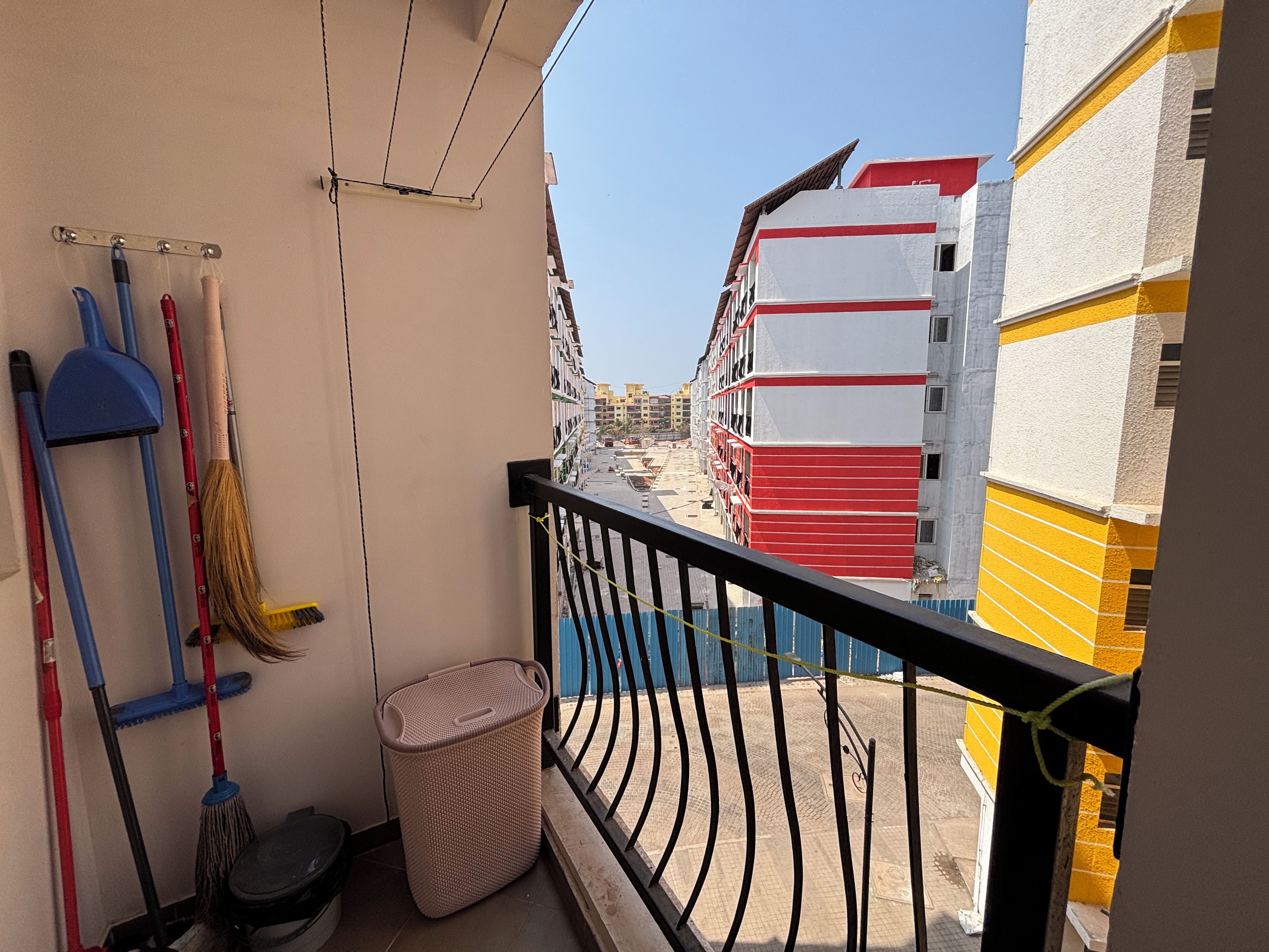 A balcony with cleaning tools, a trash bin, and a view of a building with red and white colors.