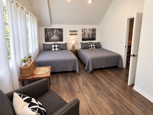 A bedroom with two beds, a sofa, a wooden chest, and a wall-mounted lamp.