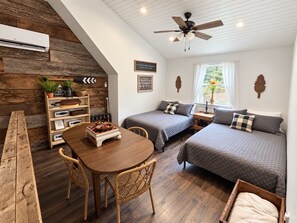 A cozy room with a wooden wall, a ceiling fan, a bed with a quilted blanket, a small table with a bowl, and a chair.